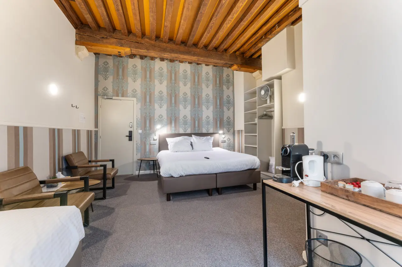 A triple room at Hotel Karel de Stoute, with a wooden-beamed ceiling, a double bed and two leather chairs
